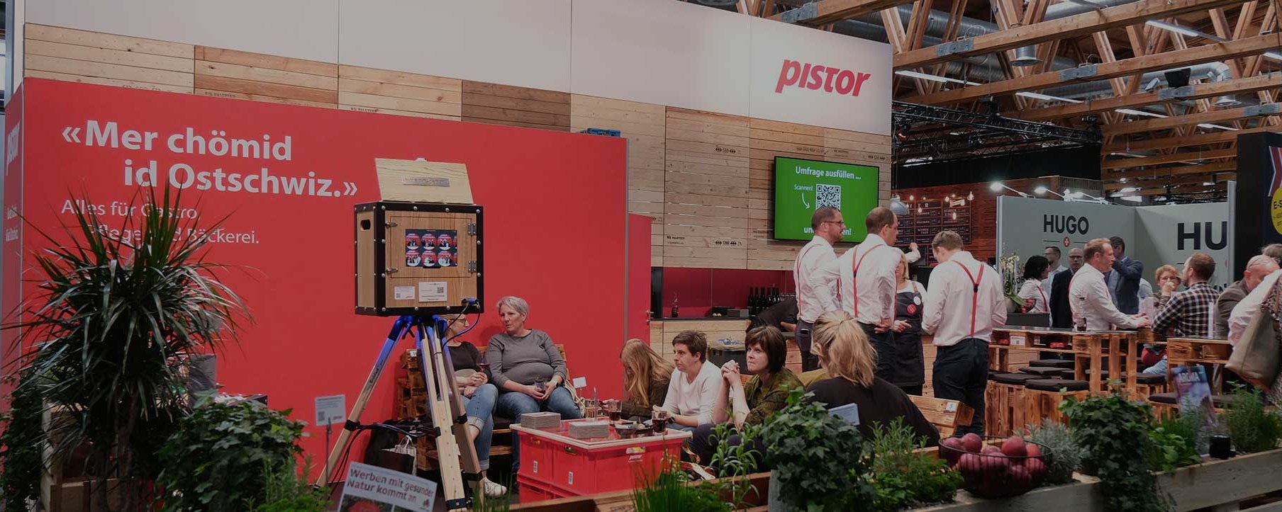 Ein Messestand mit einer roten Wand, Tischen und Menschen, die interagieren.