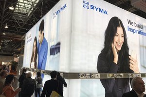 Besucher betrachten einen Messestand mit grossen, lebendigen Werbetafeln, die Menschen mit Mobiltelefonen zeigen