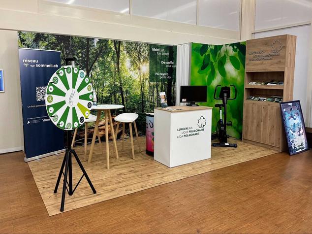 Ein Stand mit Informationsmaterialien, einem Tisch, einem Glücksrad und einem Fitnessgerät.