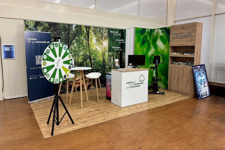 Ein Stand mit Informationsmaterialien, einem Tisch, einem Glücksrad und einem Fitnessgerät.