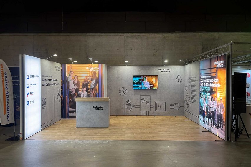 Ein Messestand von Burkhalter Bildung mit einem Empfangstresen und Informationswänden.
