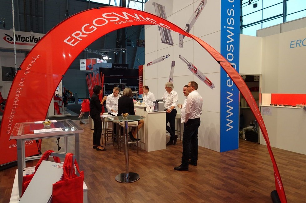 Besucher und Mitarbeiter an einem Messestand mit Markenwerbung.