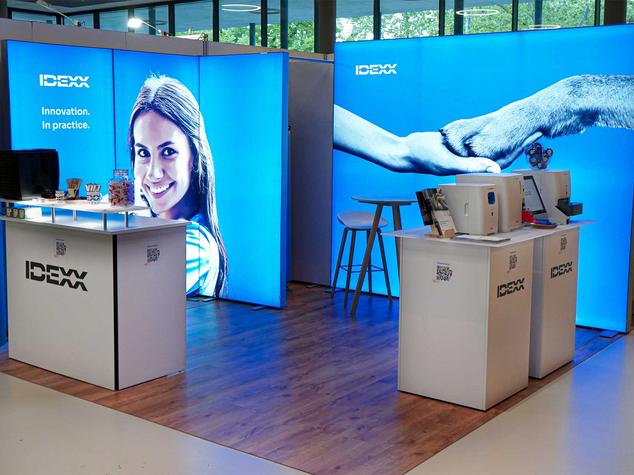 Ein Messestand mit hellblauen Wandpaneelen, einem Theke und Produkten.