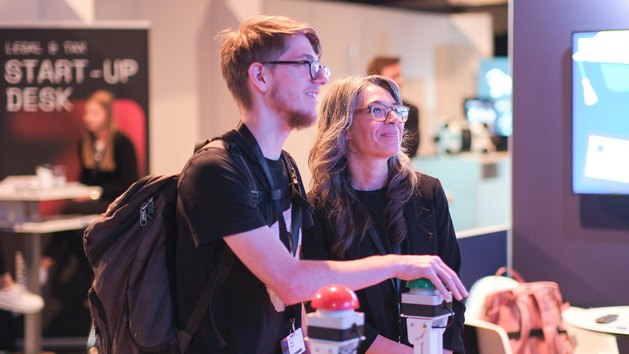Zwei Personen stehen an einem interaktiven Stand und schauen auf ein Display.
