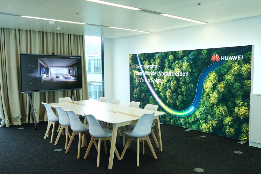 Besprechungsraum mit Tisch, Stühlen, Bildschirm und Werbebanner.