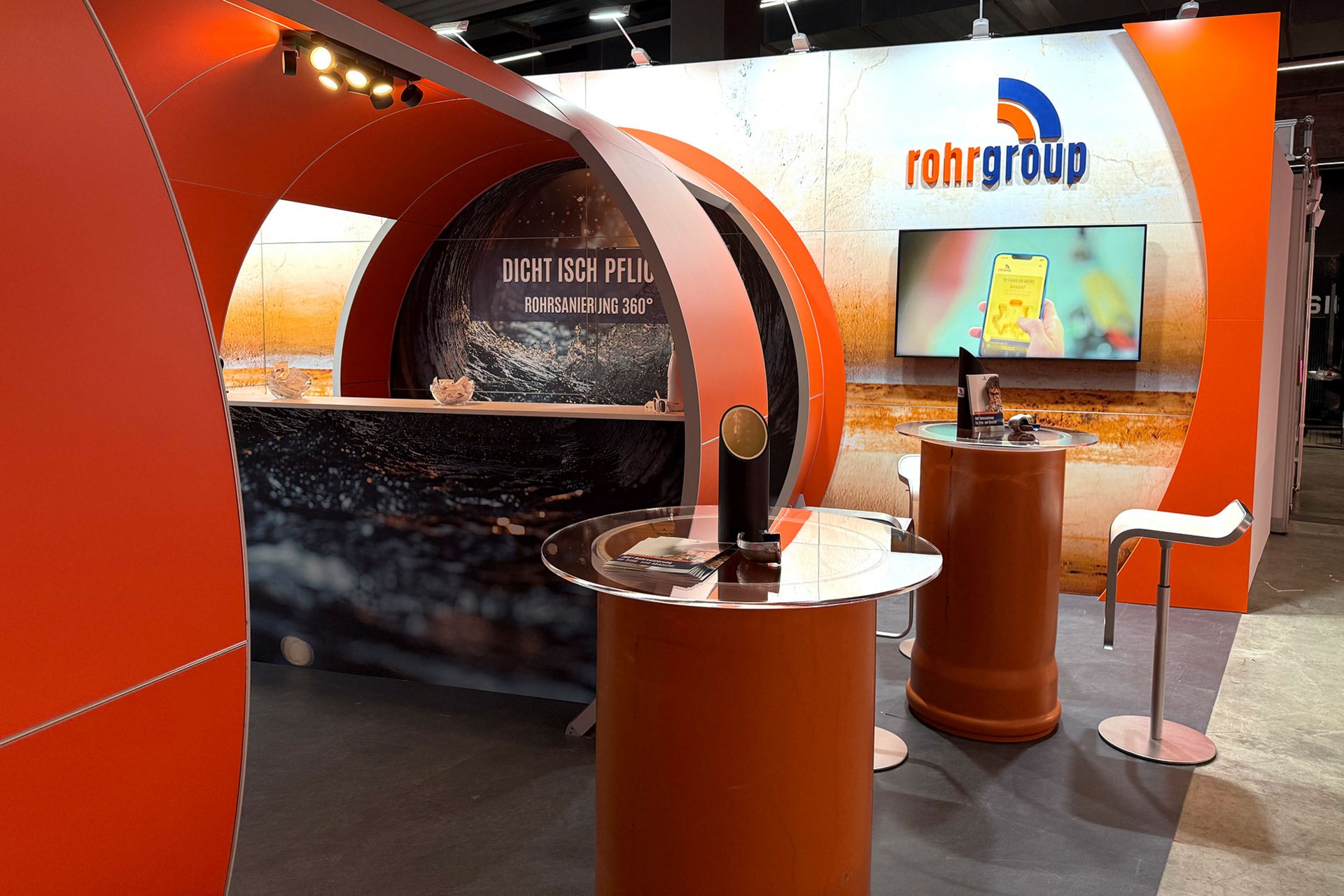 Messestand der Rohrgroup mit mehreren Theken und einem Bildschirm.