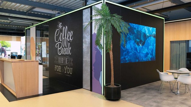 Eine Aufenthaltsraum mit einer Kaffeebar, Pflanzen und Sitzgelegenheiten.