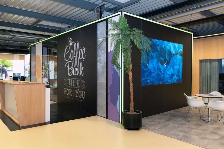 Eine Aufenthaltsraum mit einer Kaffeebar, Pflanzen und Sitzgelegenheiten.