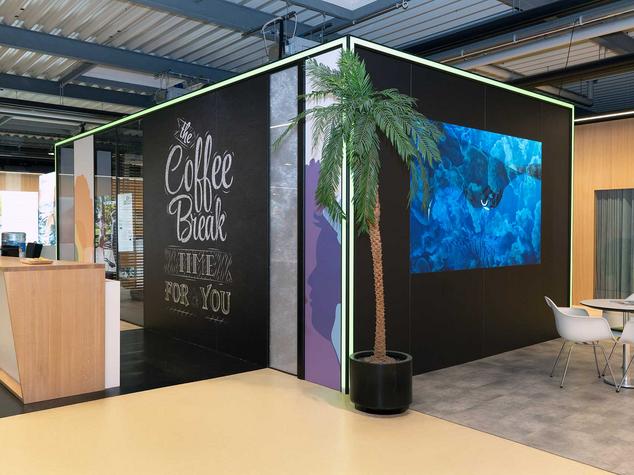 Eine Aufenthaltsraum mit einer Kaffeebar, Pflanzen und Sitzgelegenheiten.