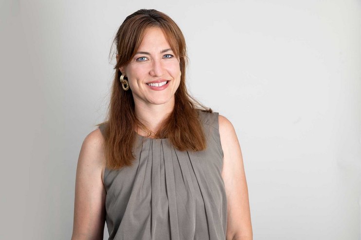 Eine Frau lächelt und trägt ein graues Oberteil.