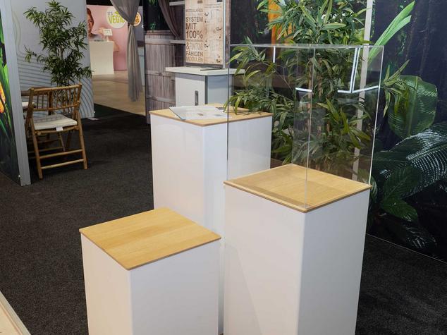 Drei Podeste mit Holzoberflächen und einer Glaskonstruktion in einem Ausstellungsraum.