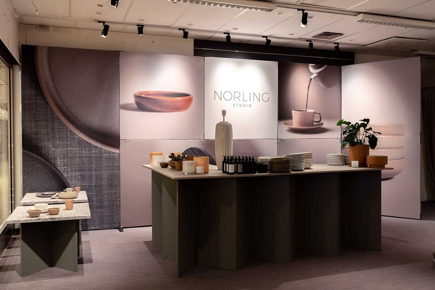 Ein Messestand mit einem Tisch, Geschirr und Hintergrundgrafiken von Keramikprodukten.