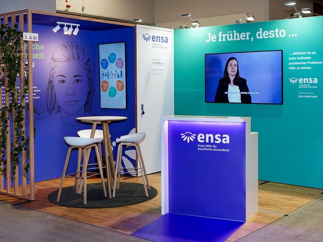 Ein Messestand mit Bildschirmen, Sitzgelegenheiten und Informationen zur psychischen Gesundheit.