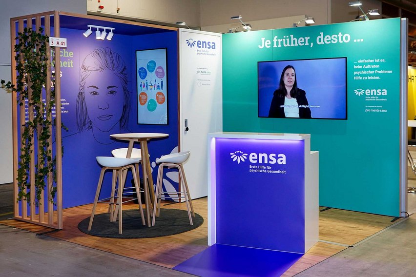 Ein Messestand mit Bildschirmen, Sitzgelegenheiten und Informationen zur psychischen Gesundheit.