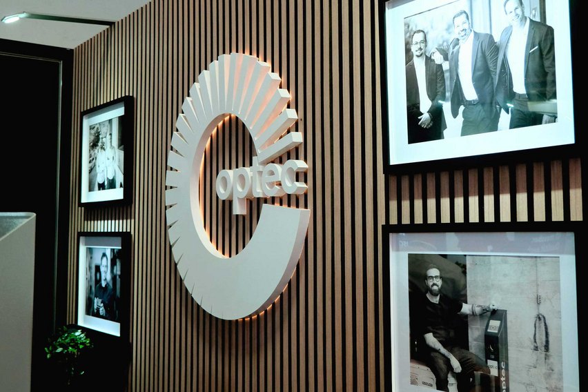 Eine Wand mit dem Logo von optec und mehreren gerahmten Schwarz-Weiss-Fotografien.
