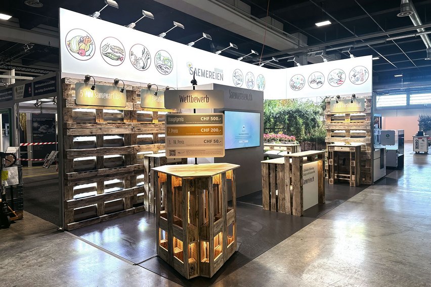 Ein Messestand mit Holzregalen und Informationen zu Samenartikeln und Wettbewerben.