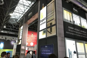 Zweistöckiger Messestand mit beleuchteten Werbetafeln und Besuchern